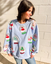 Load image into Gallery viewer, Queen of Sparkles light blue Snow Globe sequin sweatshirt with holiday snow-globe motifs, modeled with jeans outdoors