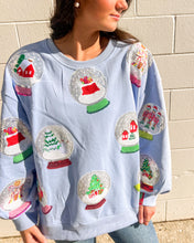 Load image into Gallery viewer, Queen of Sparkles light blue Snow Globe sequin sweatshirt with holiday snow-globe motifs, modeled with jeans outdoors