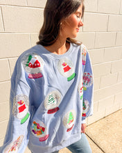 Load image into Gallery viewer, Queen of Sparkles light blue Snow Globe sequin sweatshirt with holiday snow-globe motifs, modeled with jeans outdoors