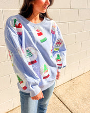Load image into Gallery viewer, Queen of Sparkles light blue Snow Globe sequin sweatshirt with holiday snow-globe motifs, modeled with jeans outdoors