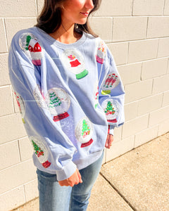 Queen of Sparkles light blue Snow Globe sequin sweatshirt with holiday snow-globe motifs, modeled with jeans outdoors