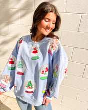 Load image into Gallery viewer, Queen of Sparkles light blue Snow Globe sequin sweatshirt with holiday snow-globe motifs, modeled with jeans outdoors